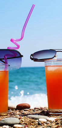 A Rocky Beach with Waves Crashing Behind Two Glasses of Pirate Rum Punch